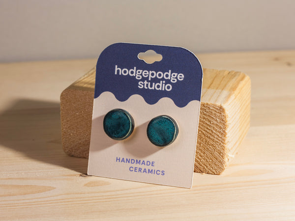 Blue ceramic earrings on a 'hodgepodge studio' card against a wooden background
