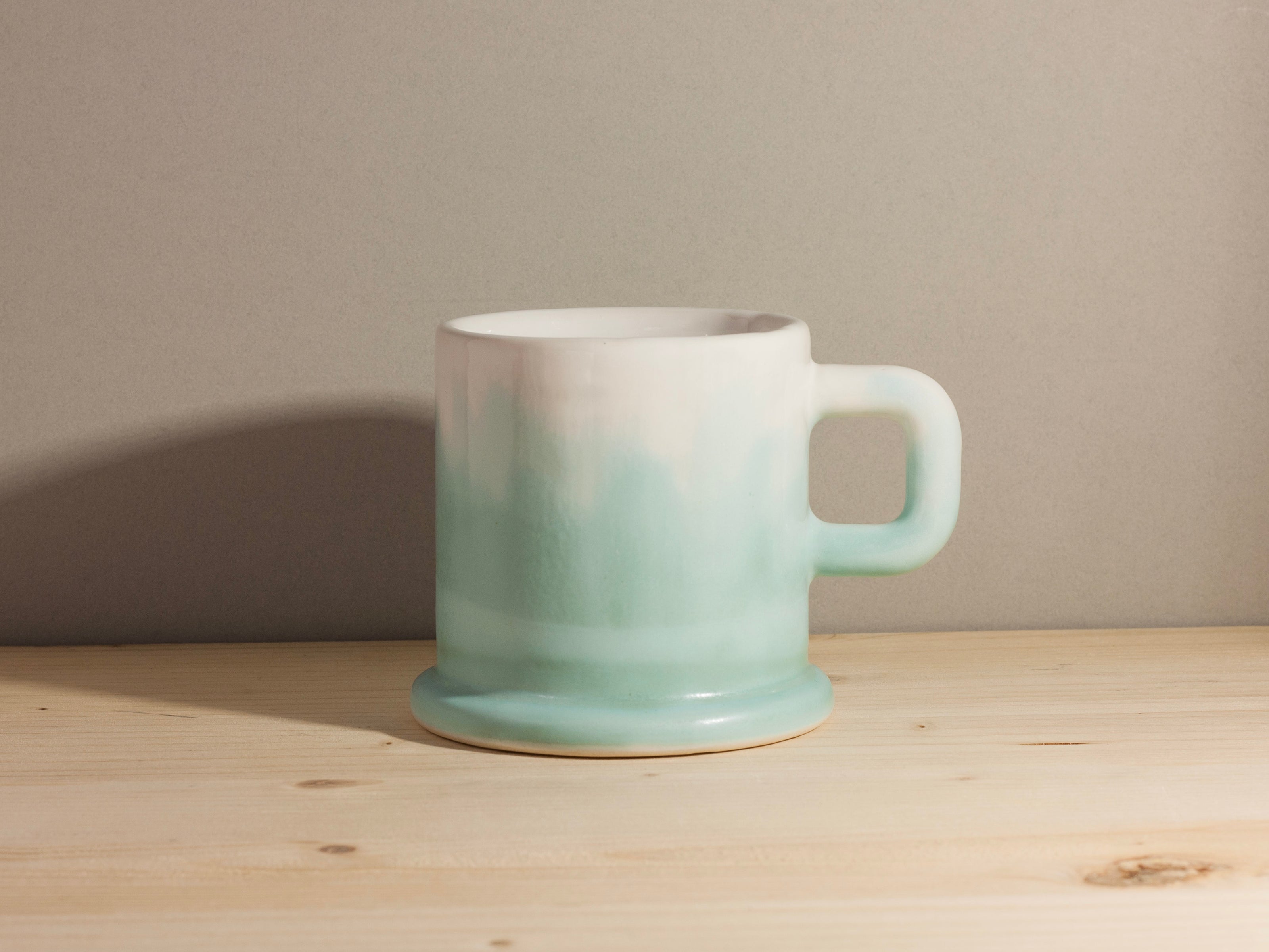 Ceramic mug with gradient color from white to green on a wooden surface.