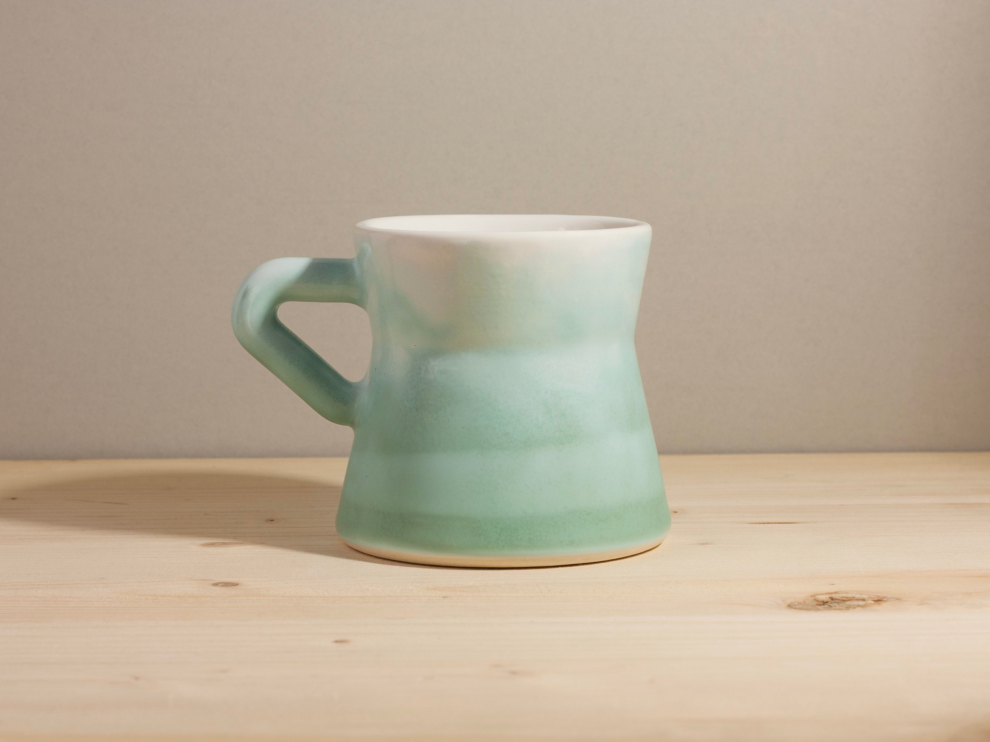 Blue green ceramic mug on a wooden surface with a neutral background