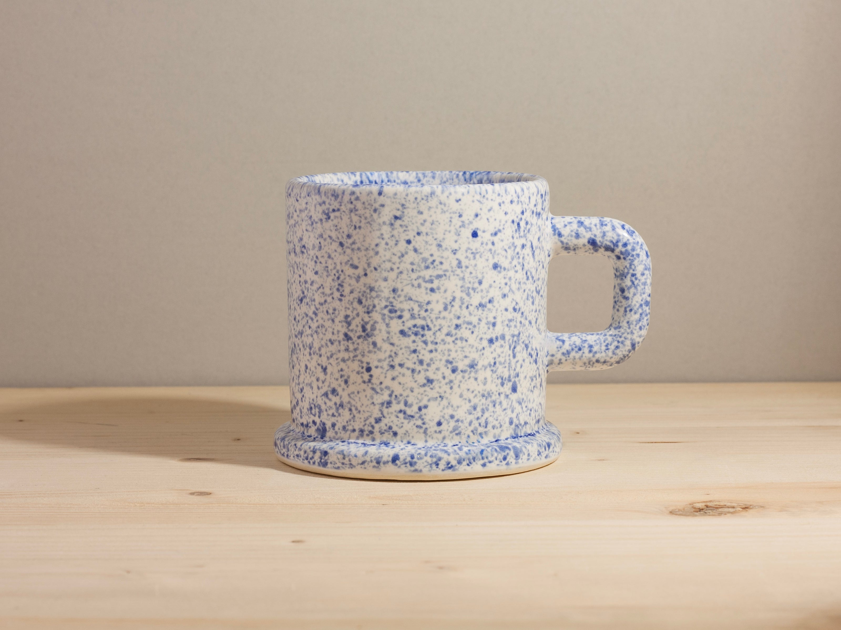Speckled blue and white ceramic mug on a wooden surface with a beige background