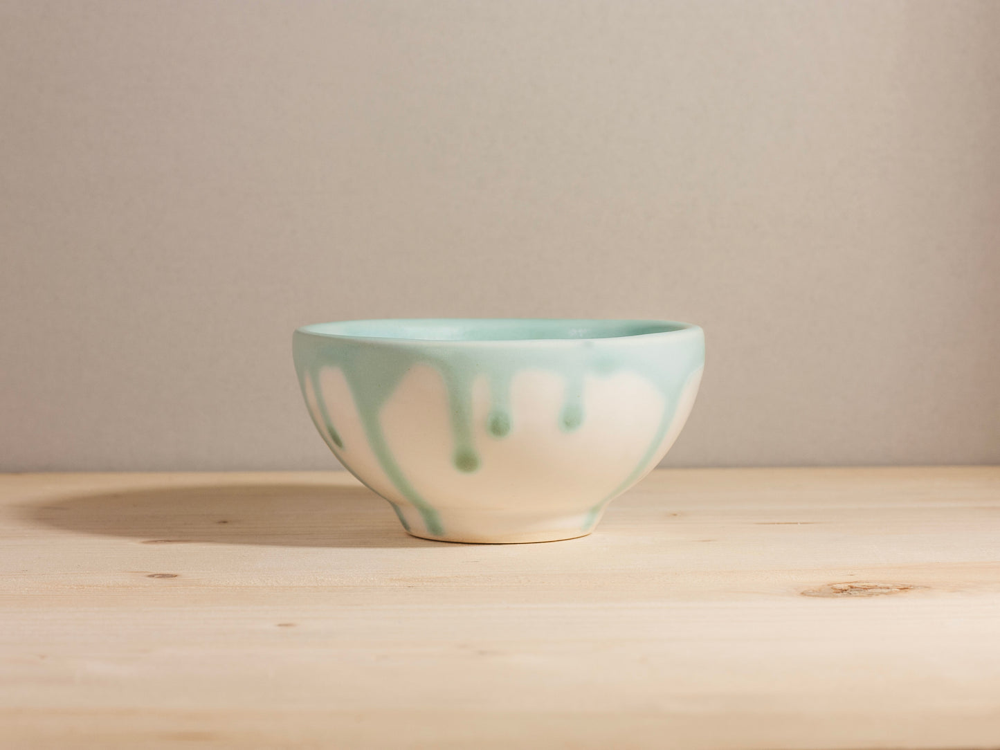 Ceramic bowl with dripping design on a wooden surface and beige background