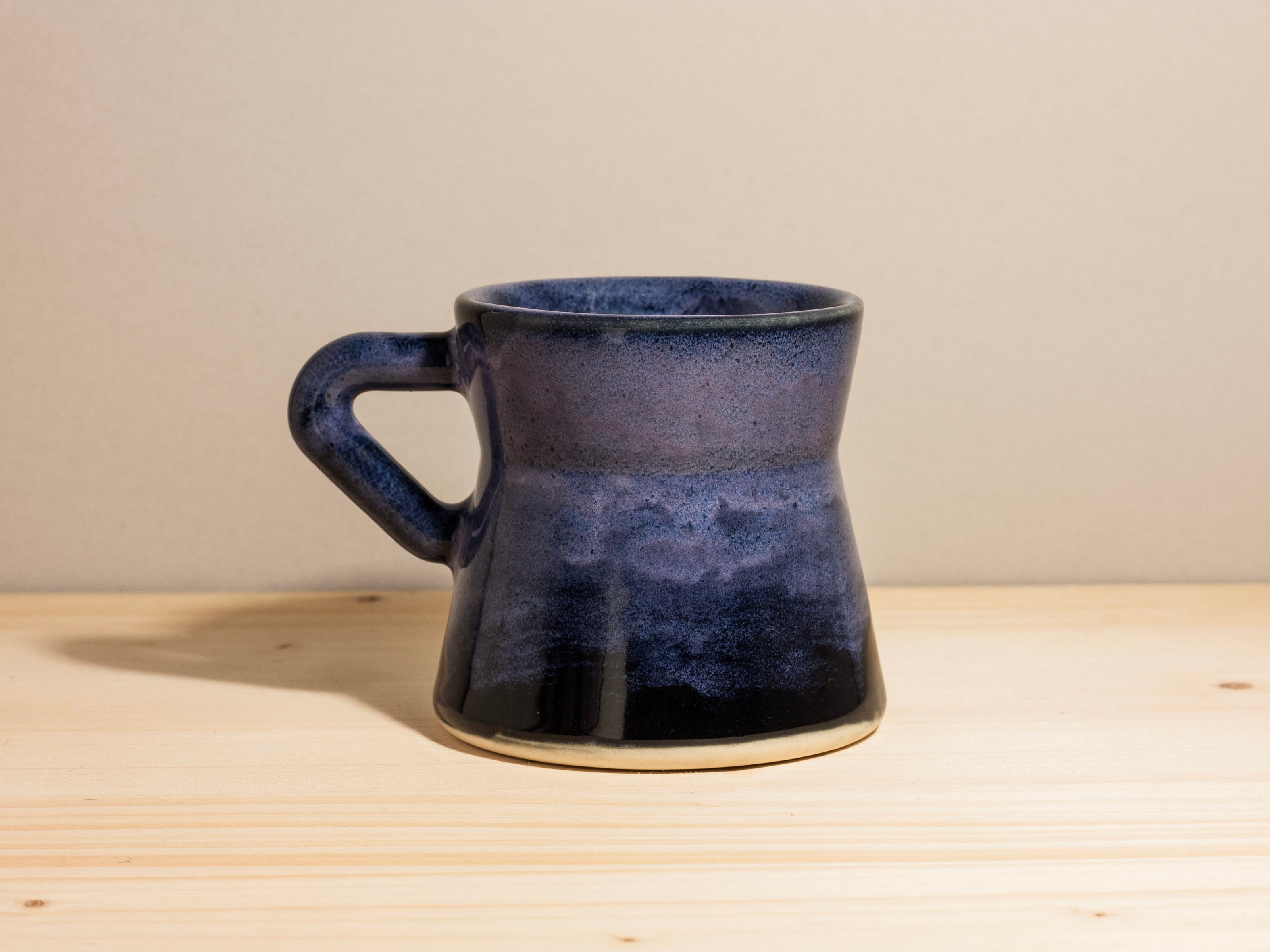 Dark purple ceramic mug on a wooden surface with a plain background