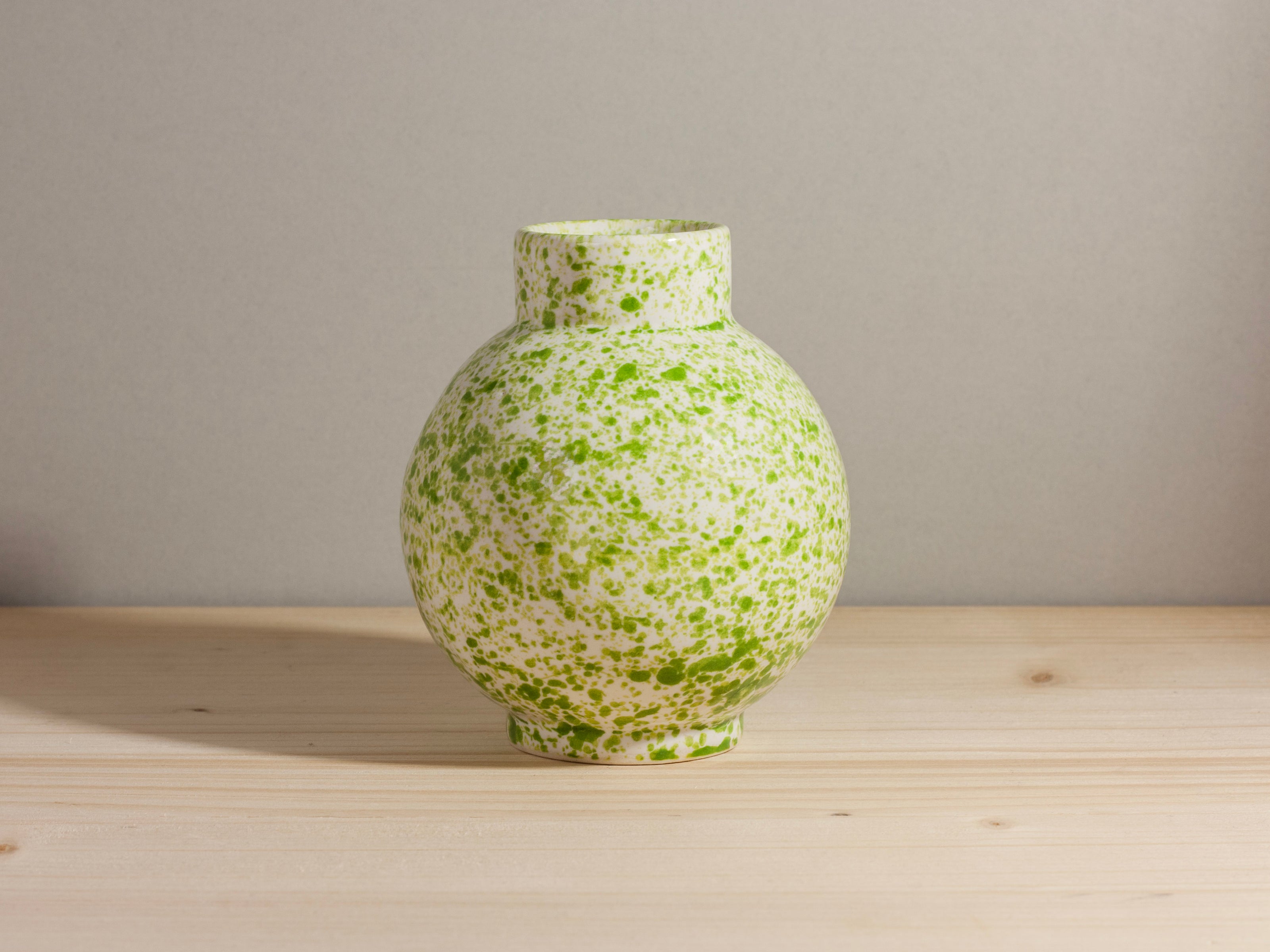Green speckled vase on a wooden surface with a gray background