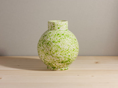 Green speckled vase on a wooden surface with a gray background
