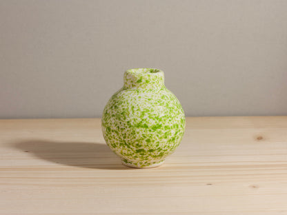 Green speckled vase on a wooden surface with a neutral background