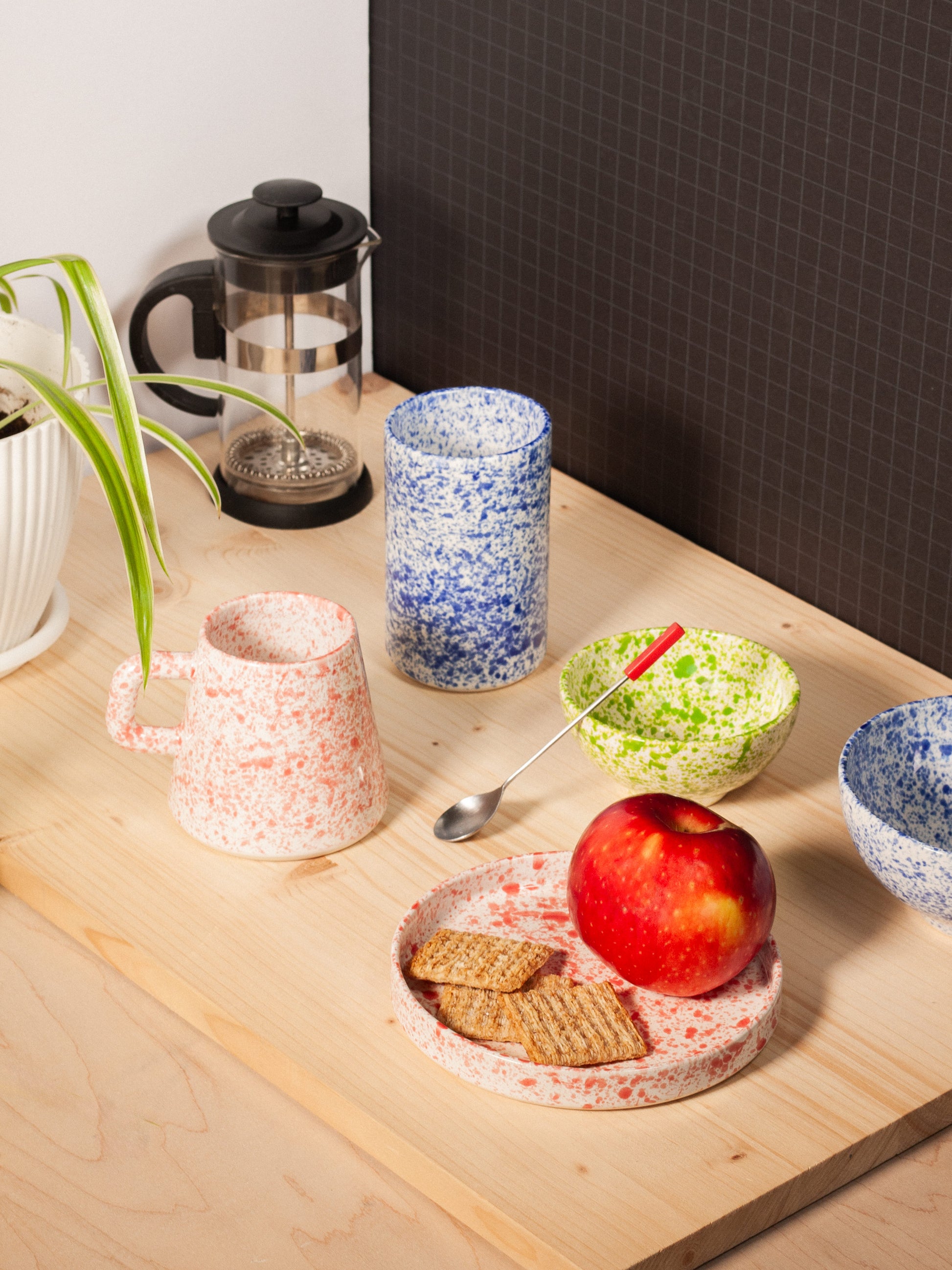Speckled ceramic items including cups, a bowl, and a plate on a wooden surface.