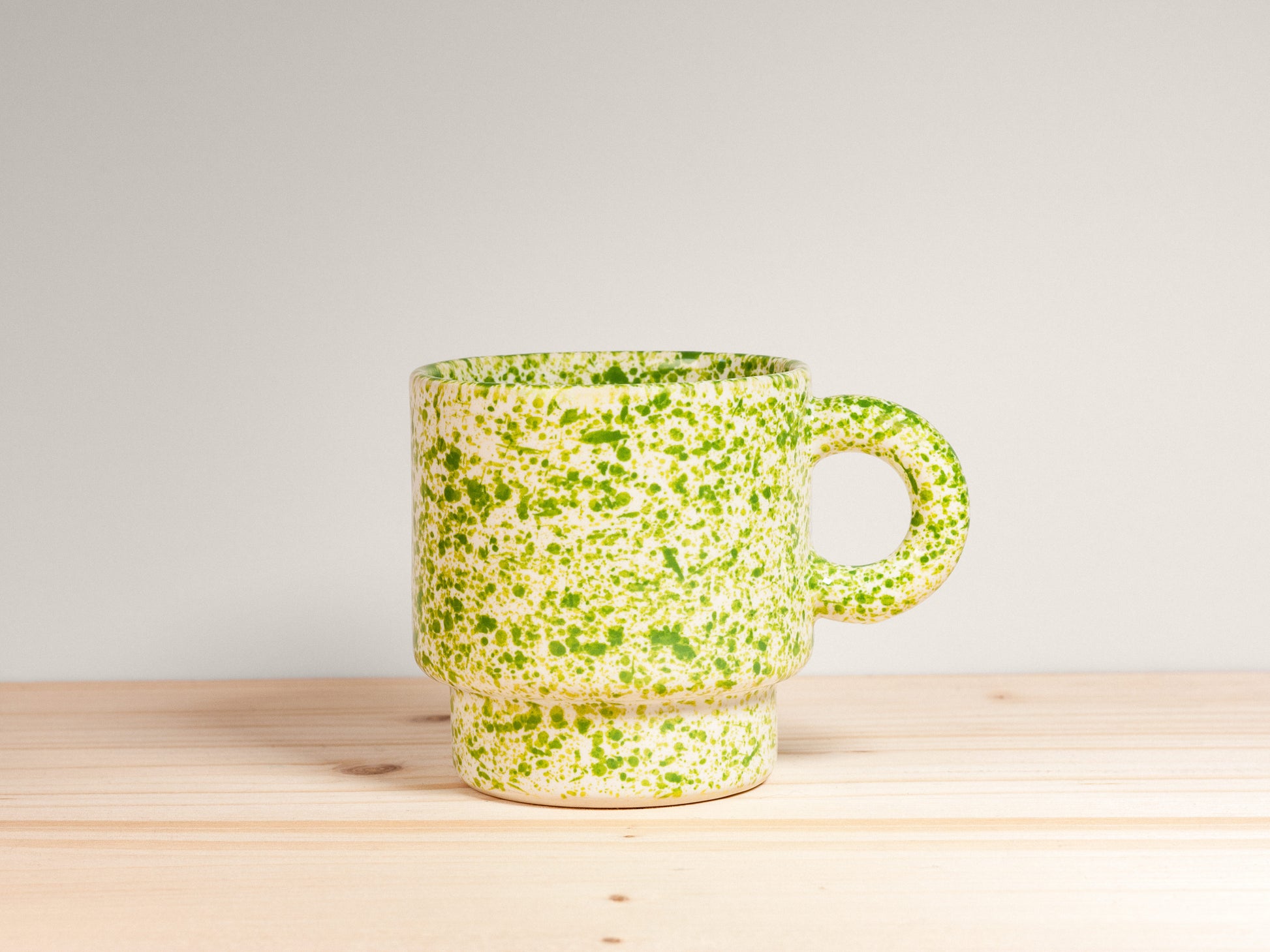Green speckled ceramic mug on a wooden surface with a light gray background