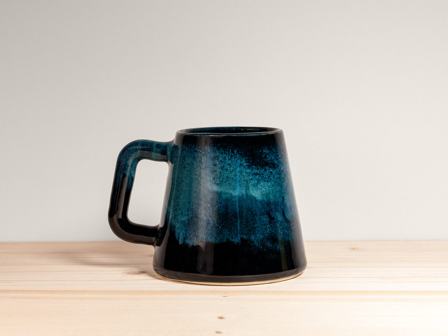 Dark teal ceramic mug on a wooden surface with a plain background.