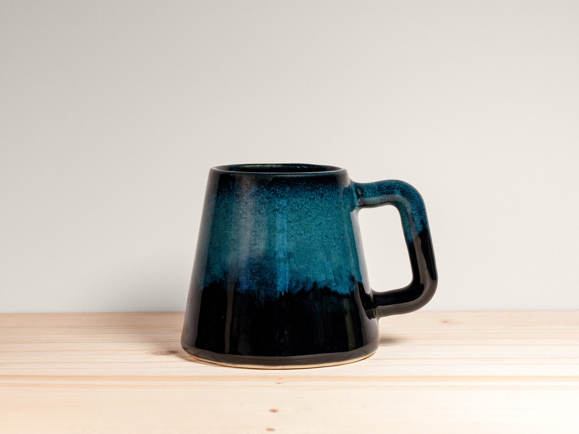 Dark teal ceramic mug on a wooden surface with a plain background.