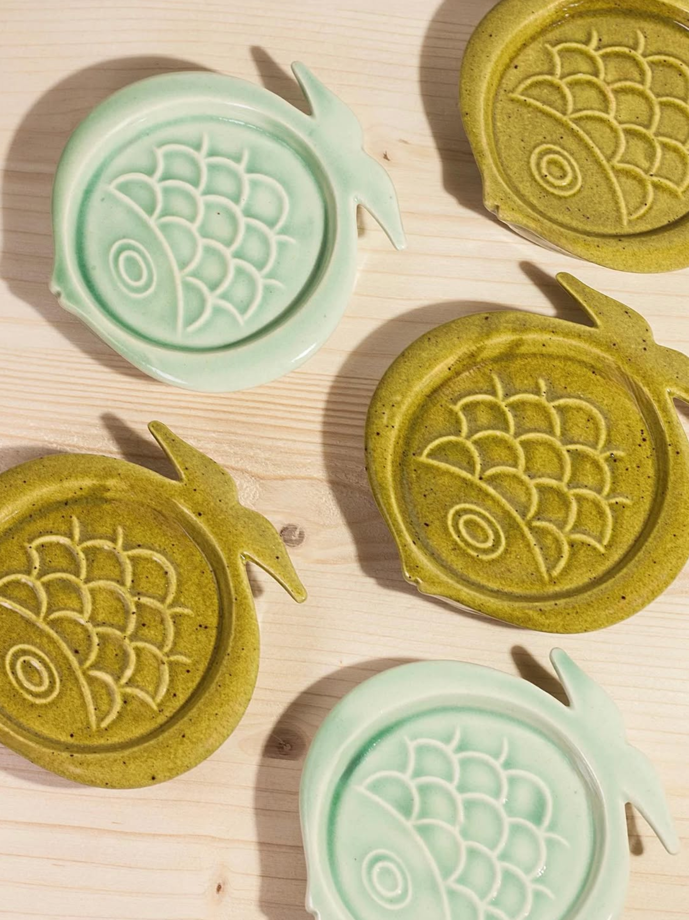 Green and light green ceramic coasters with fish design on a wooden surface